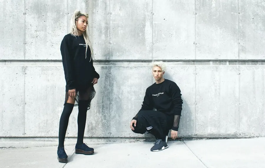 Pareja con sudaderas negras frente a un muro de concreto