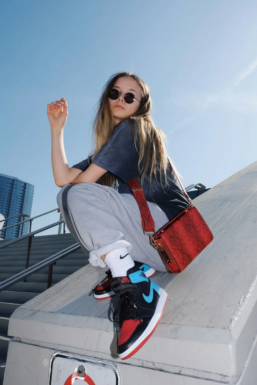 Chica con sneakers y bolso rojo sentada en unas escaleras